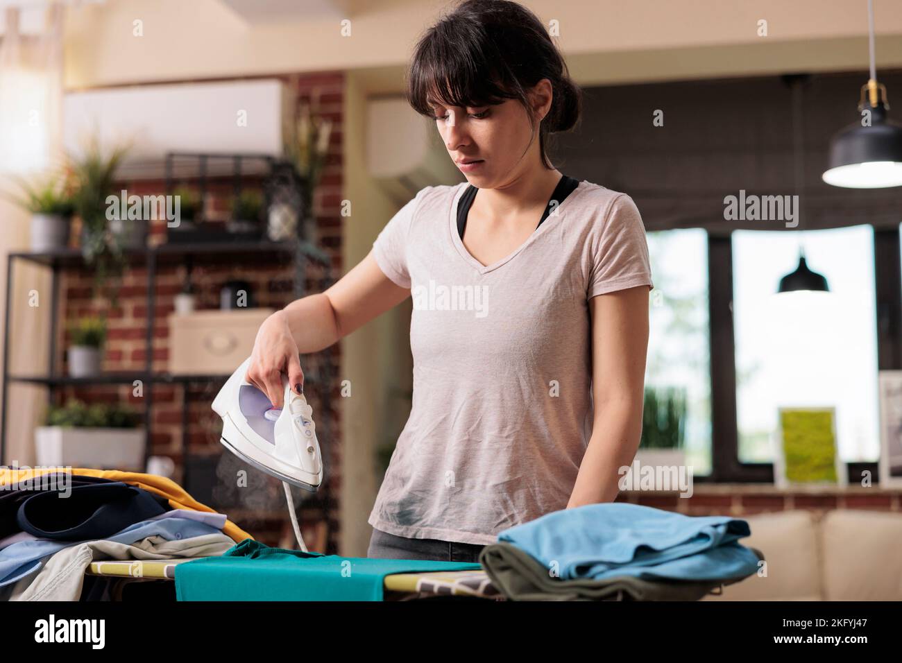 Modern woman concentrating while ironing clothes at home after doing