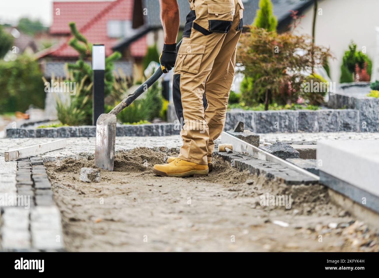 Professional Construction Worker Evenly Spreading Sand with a Shovel Before Laying Paving Bricks. Garden Walkway Building Process. Stock Photo