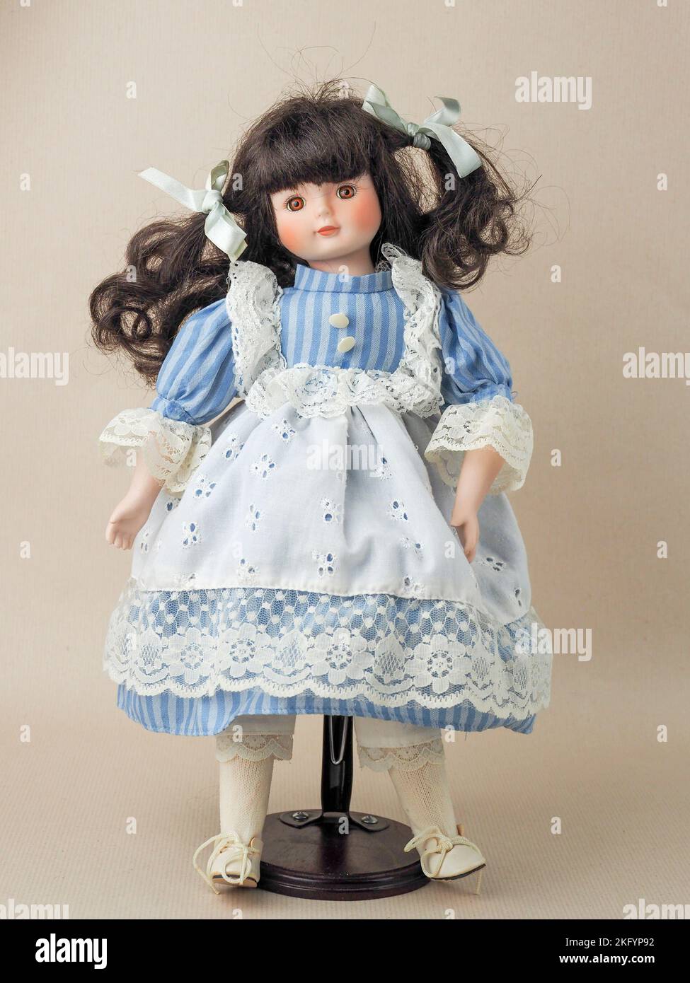 Garham, Germany. 18th Nov, 2022. In this photo illustration, a vintage porcelain doll girl with brown eyes brunette with braided ribbons in a blue dress with white vertical stripes and a lace apron. Porcelain dolls appeared in the 18th century in France. They were used to promote French fashion in the world. Usually such dolls were supplied with a large number of clothes and sent to customers as mini mannequins. (Credit Image: © Igor Golovniov/SOPA Images via ZUMA Press Wire) Stock Photo