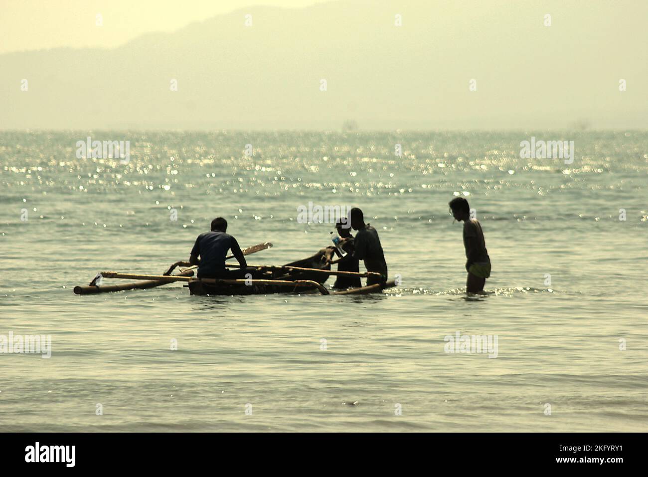 Men preparing an outrigger canoe for national park visitors on the coastal water of Handeuleum Island, a part of Ujung Kulon National Park in Pandeglang, Banten, Indonesia. Stock Photo