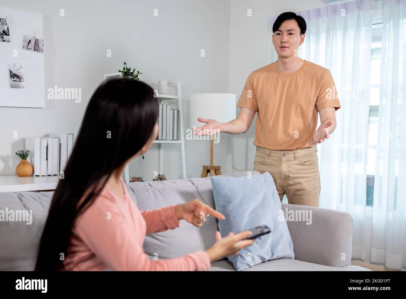 Shocked jealous Asian girlfriend suspecting infidelity by reading text messages on her cheating boyfriend's phone at home. Wife checking husband's smartphone and having jealousy problem Stock Photo
