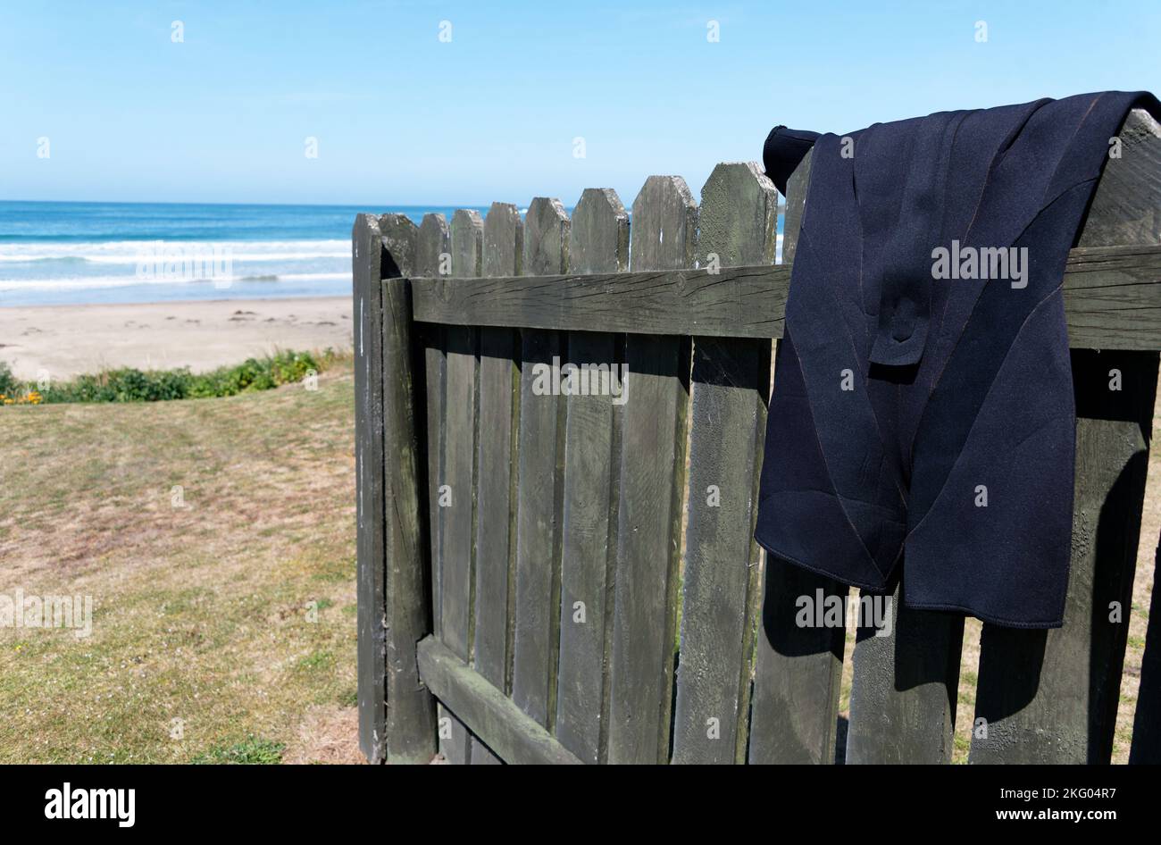 A shorty wetsuit is hanging on a fence to dry, its been having fun in the sea nearby. Stock Photo