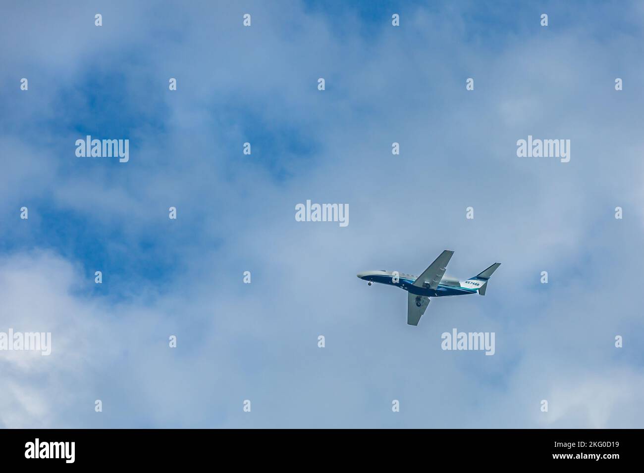A blue and white 2010 Cessna 525c commuter plane in flies overhead. Stock Photo