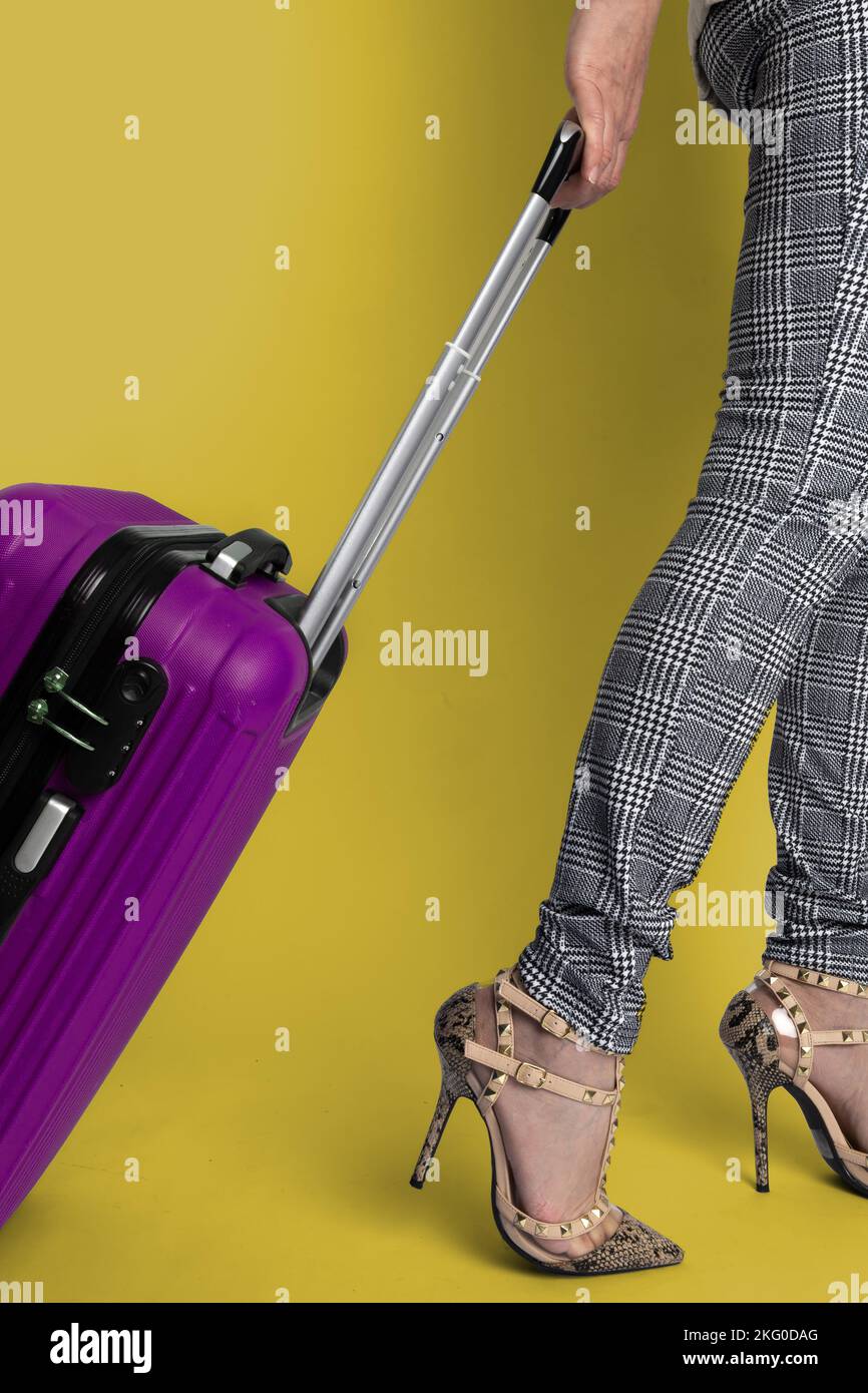 Half lower body of girl pulling a purple suitcase with a yellow background. Stock Photo