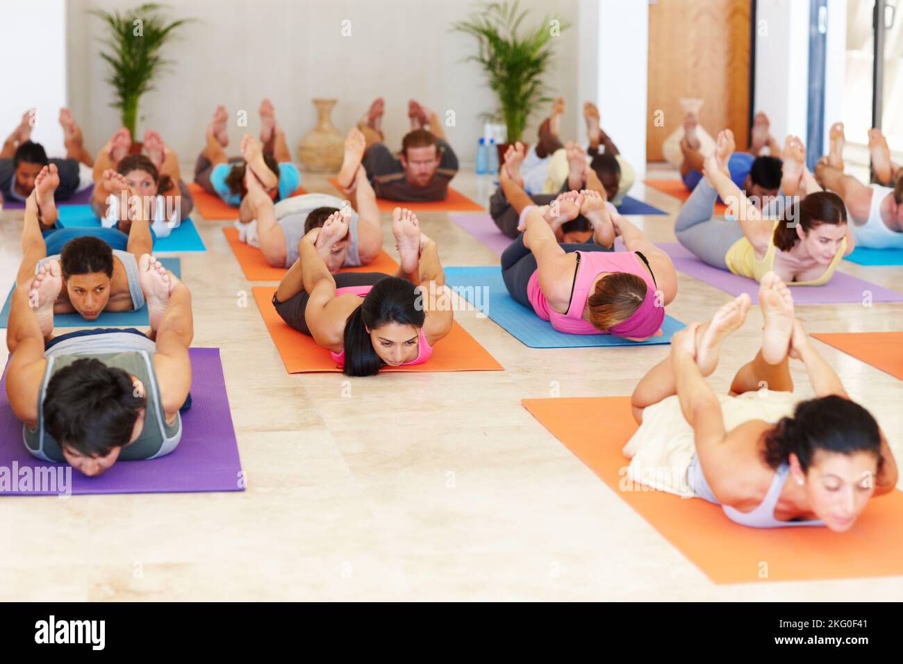 Performing the bow pose. A yoga class lying on their stomachs and pulling their legs over their backs. Stock Photo