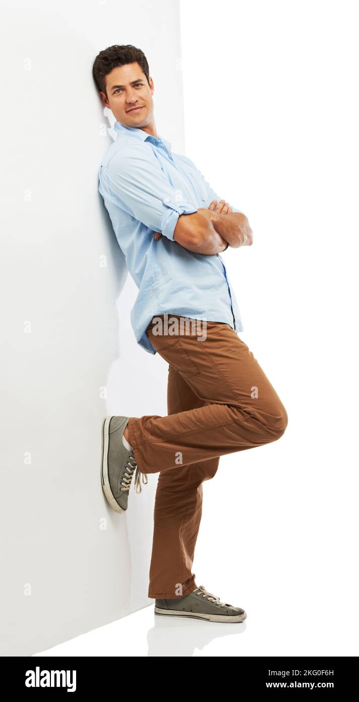 Casual fashion in studio. A handsome young man leaning against a wall while isolated on a white background. Stock Photo