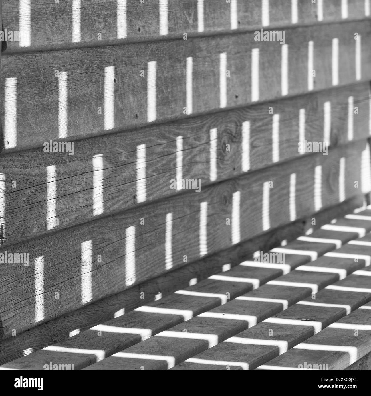 Low contrast black and white photo of the sunlight making patterns on a bench Stock Photo