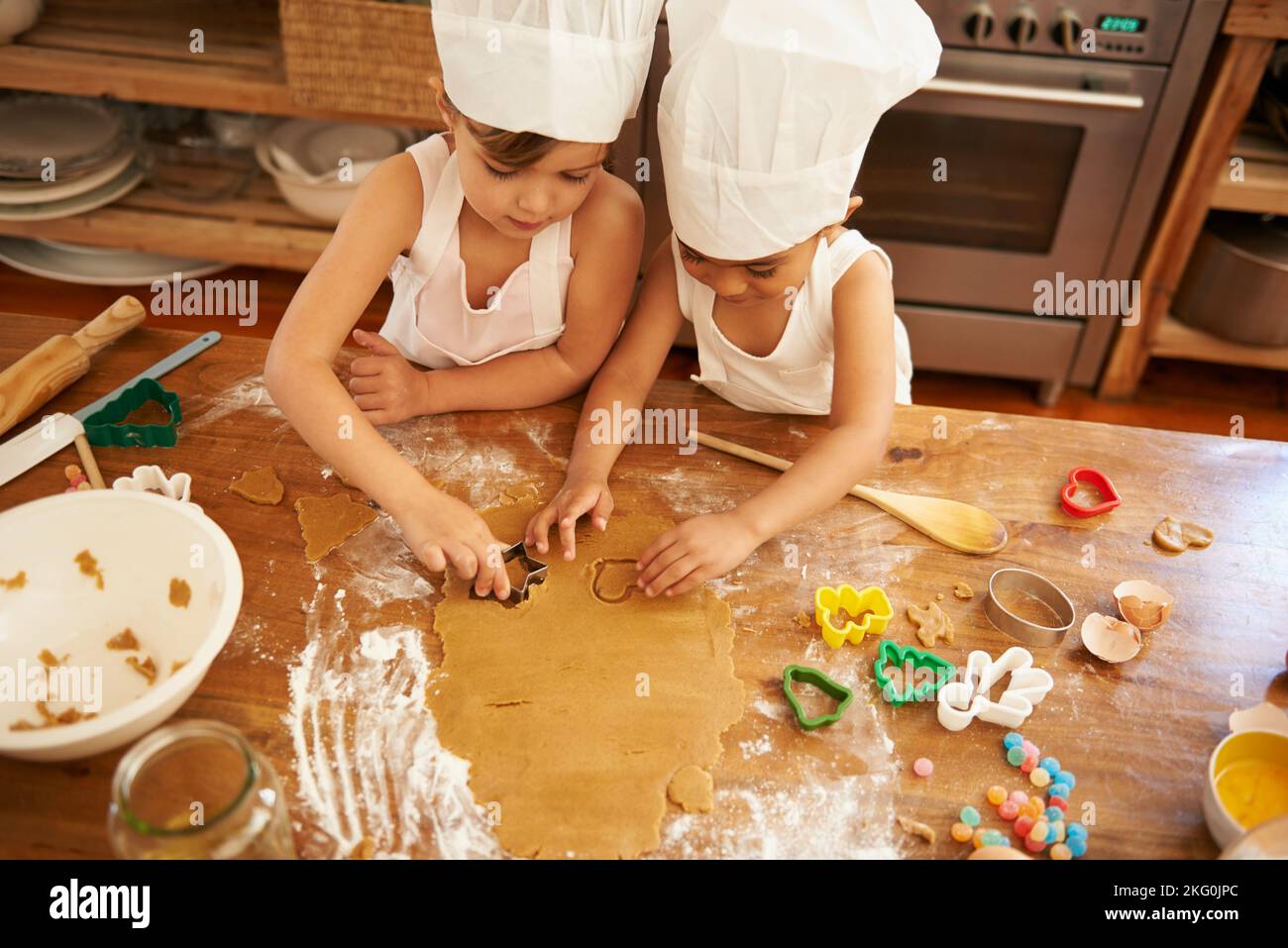 Family, baking and children learning to shape cookies at a table, development and bond in a kitchen. Cake, cutter and boy kids having fun while making Stock Photo