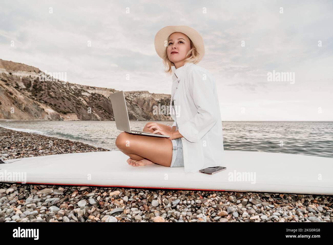 Digital nomad, Business woman working on laptop by the sea. Pretty lady typing on computer by the sea at sunset, makes a business transaction online Stock Photo