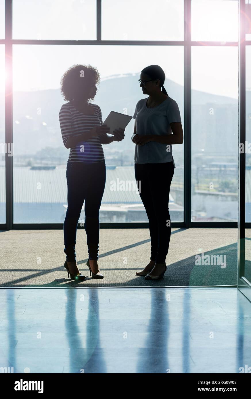 Ideas exchanged on the go. Silhouette shot of female coworkers talking while standing in front of a window in an office. Stock Photo