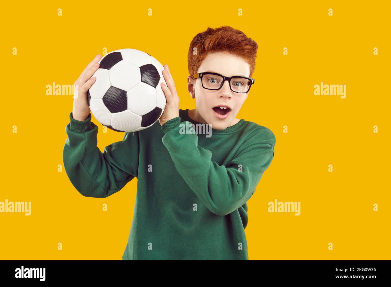 Shocked preteen boy catches black and white soccer ball, isolated on orange background. Stock Photo