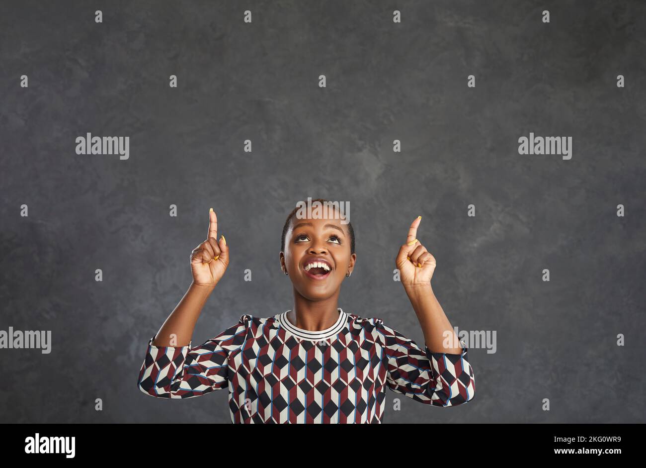 Dark skinned woman looks up and with her index finger pointing up offers something to choose from. Stock Photo