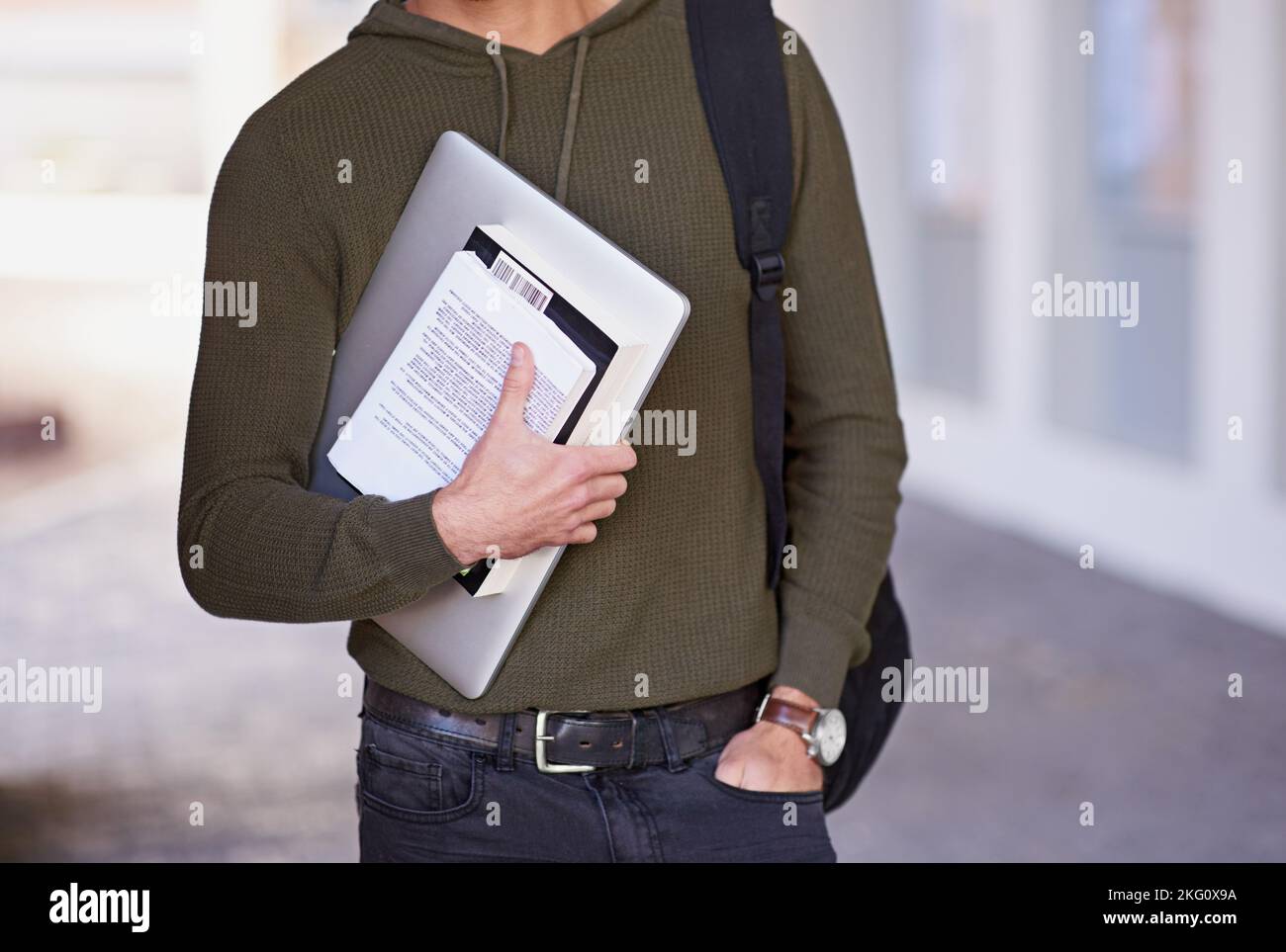 Education is the key to success. a male student carrying books and a laptop while standing outside. Stock Photo