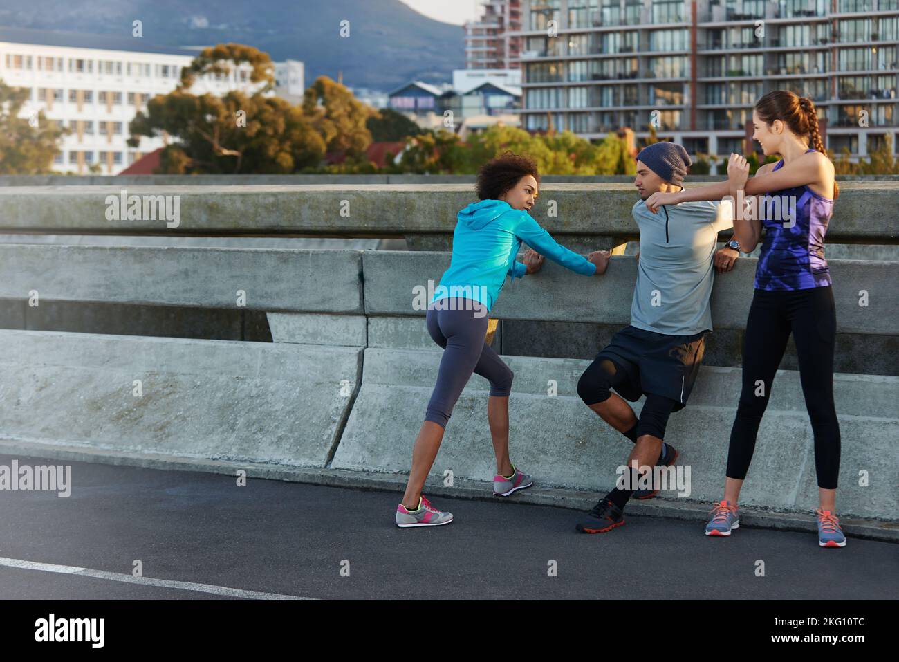 Stetching before their morning run. three friends stretching at the road side before a morning jog. Stock Photo