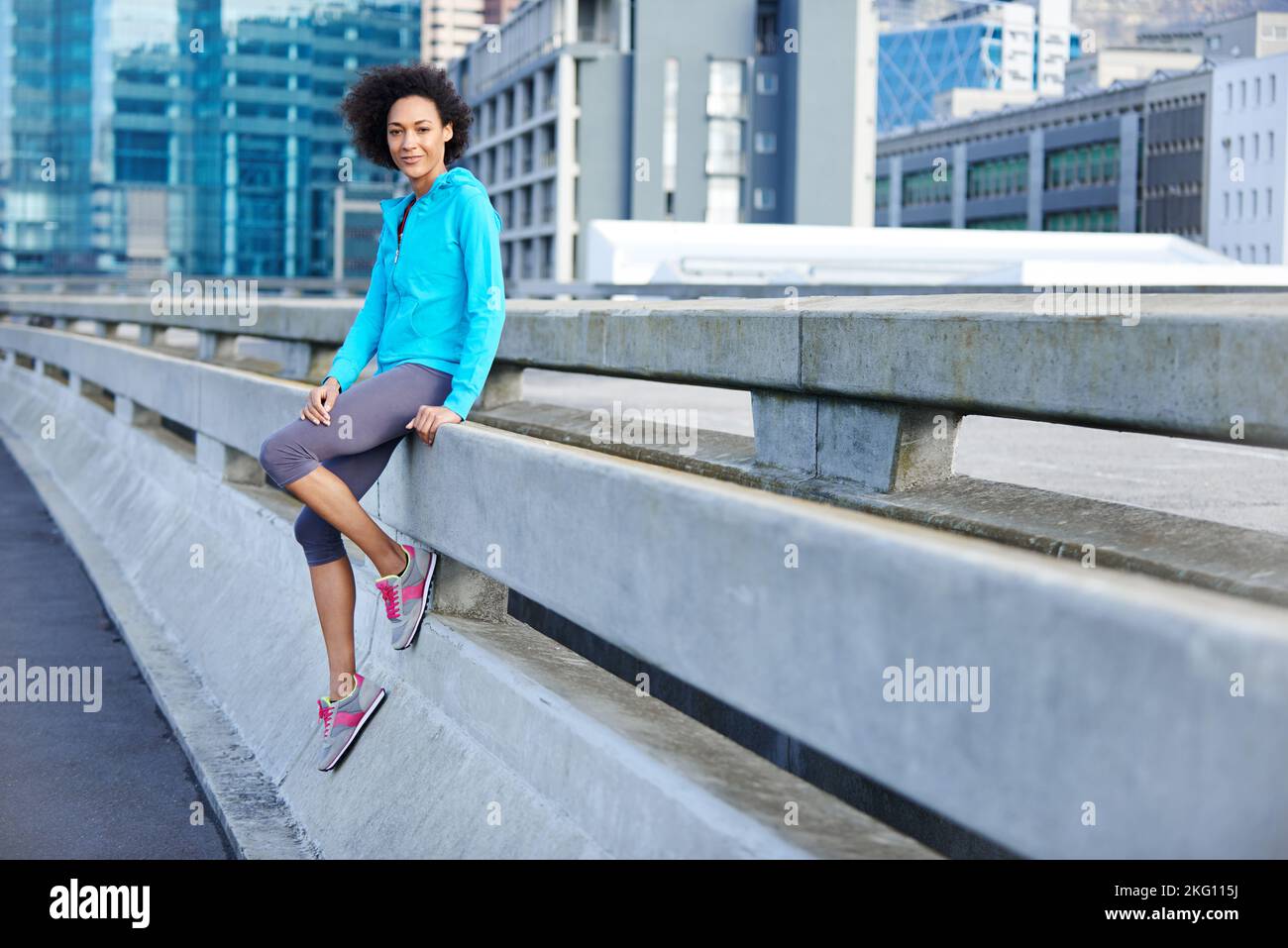 Enjoying a mid-run break. Portrait of a young female jogger leaning against a road railing in the city. Stock Photo