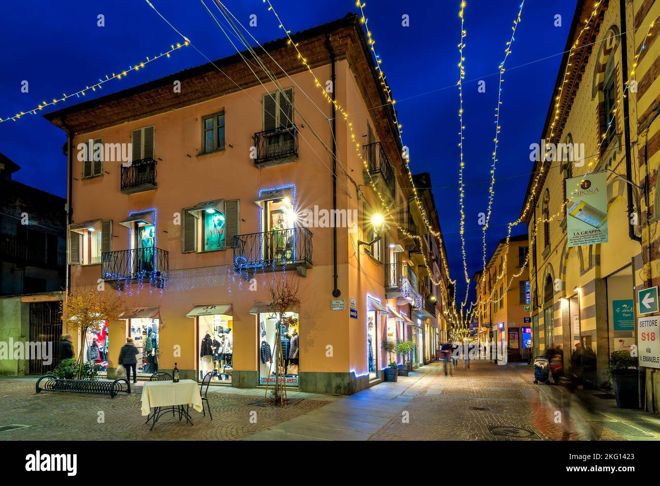People on the cobblestone pedestrian street illuminated with Christmas lights among old buildings in Alba, Italy. Stock Photo