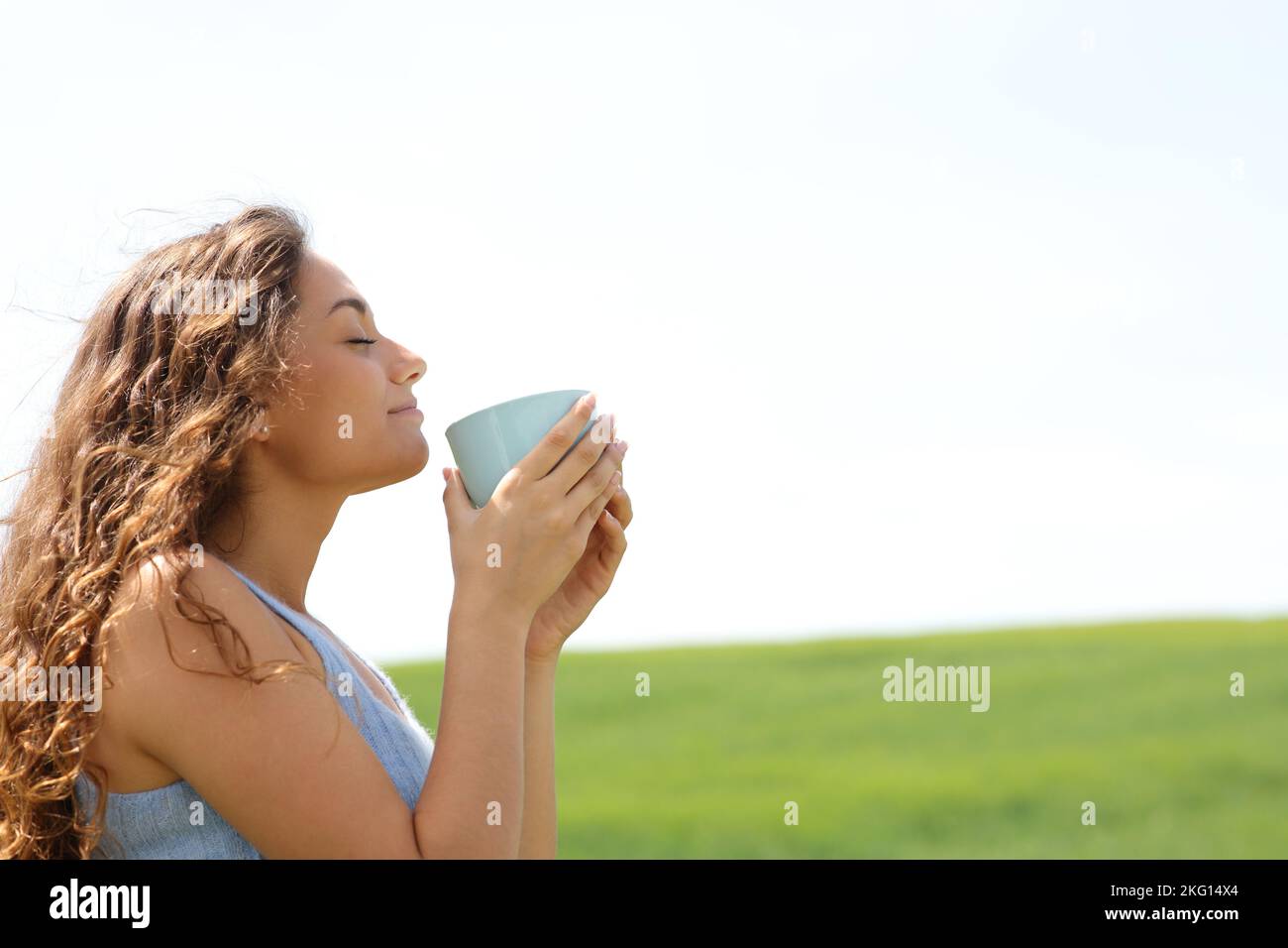 Side view portrait of a woman smelling coffee in a field Stock Photo
