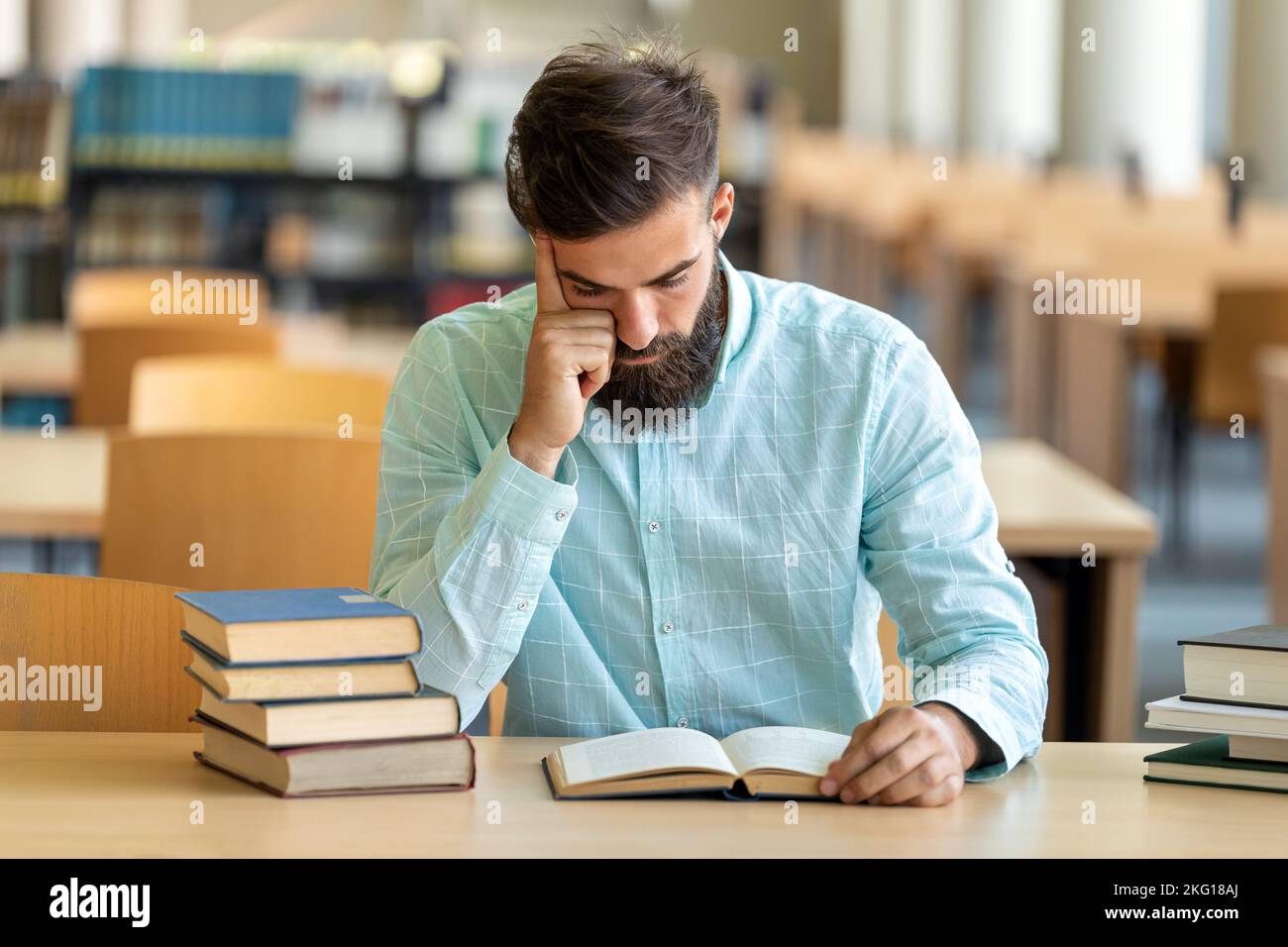 Exhausted young male studying and preparing for exam in college library. Education people concept Stock Photo