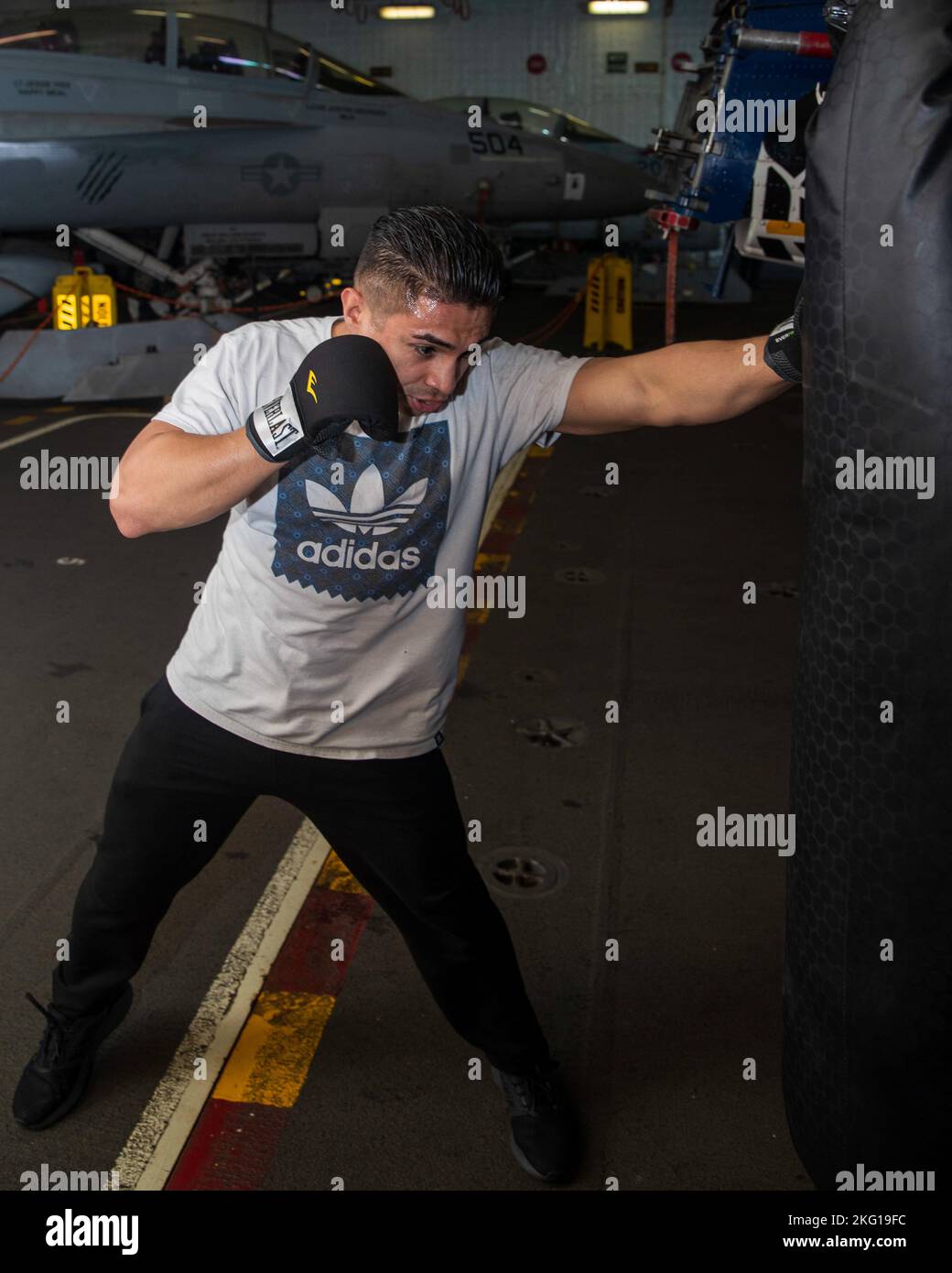 Aviation Structural Mechanic 3rd Class Luis Calderon, from Fort Worth, Texas, assigned to the “Golden Warriors” of Strike Fighter Squadron (VFA) 87, punches a punching bag in the first-in-class aircraft carrier USS Gerald R. Ford's (CVN 78) hangar bay, Oct. 21, 2022. The Gerald R. Ford Carrier Strike Group (GRFCSG) is deployed in the Atlantic Ocean, conducting training and operations alongside NATO Allies and partners to enhance integration for future operations and demonstrate the U.S. Navy’s commitment to a peaceful, stable and conflict-free Atlantic region. Stock Photo