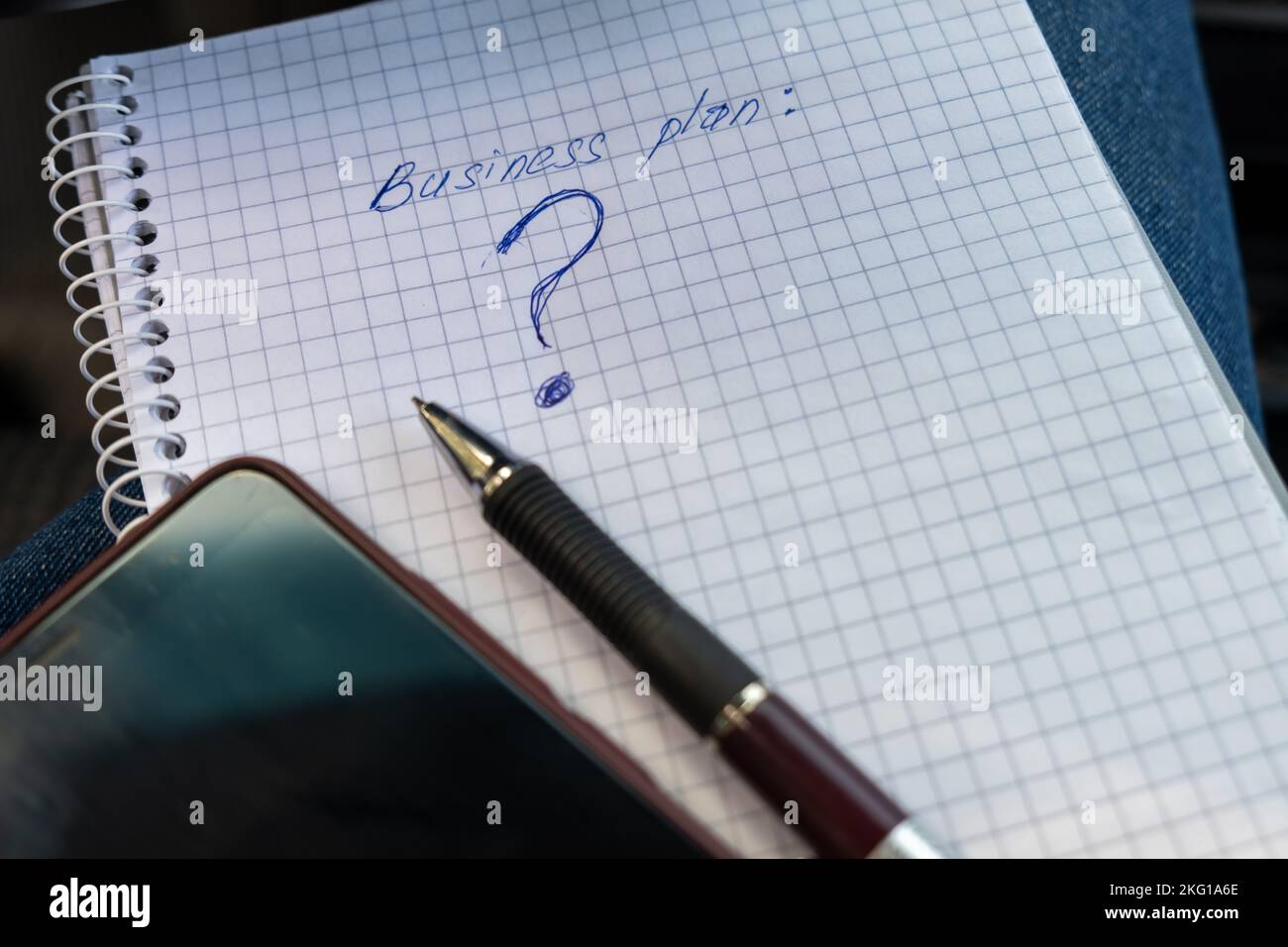 Business plan and question mark written on a notebook. Reflections on enrichment, entrepreneurship. Stock Photo