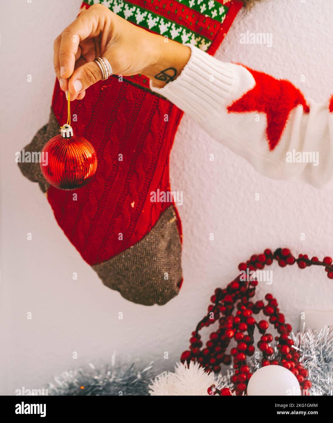 Christmas holiday season and home decoration concept image. Woman hands holding xmas ball with sock in background. Red december color concept. Home wa Stock Photo
