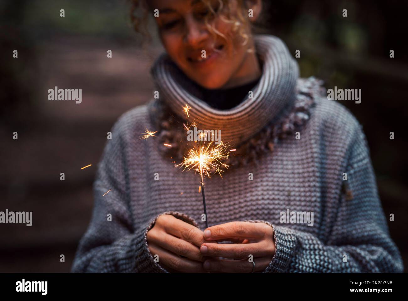 Front view of happy woman celebrating with sparkler light in outdoor. Foreground focus on fire and female people smiling in background. New year eve a Stock Photo