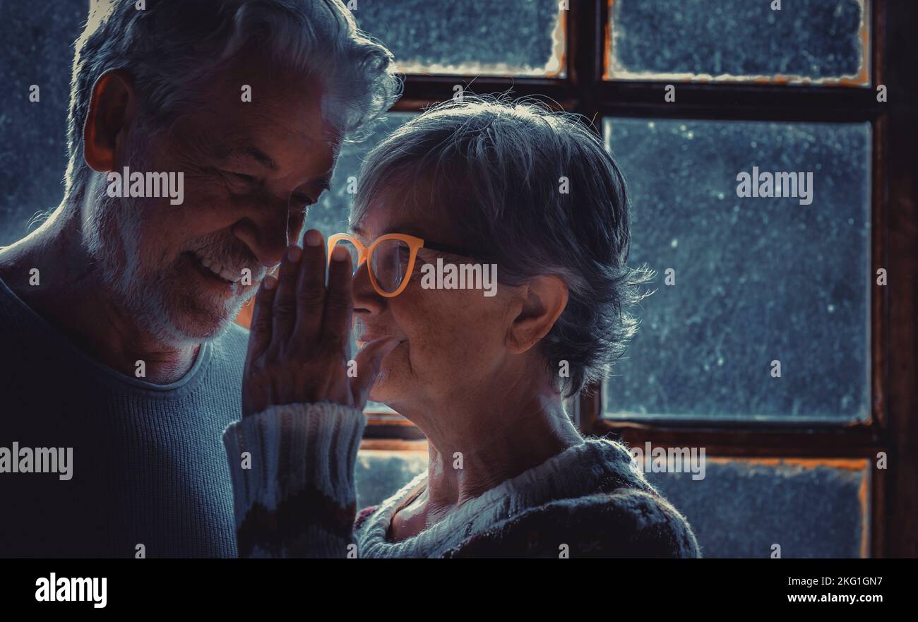 Senior woman whispering at her mature husband at home. Old aged couple in love and relationship. Telling secrets. Portrait of retired elderly lifestyl Stock Photo