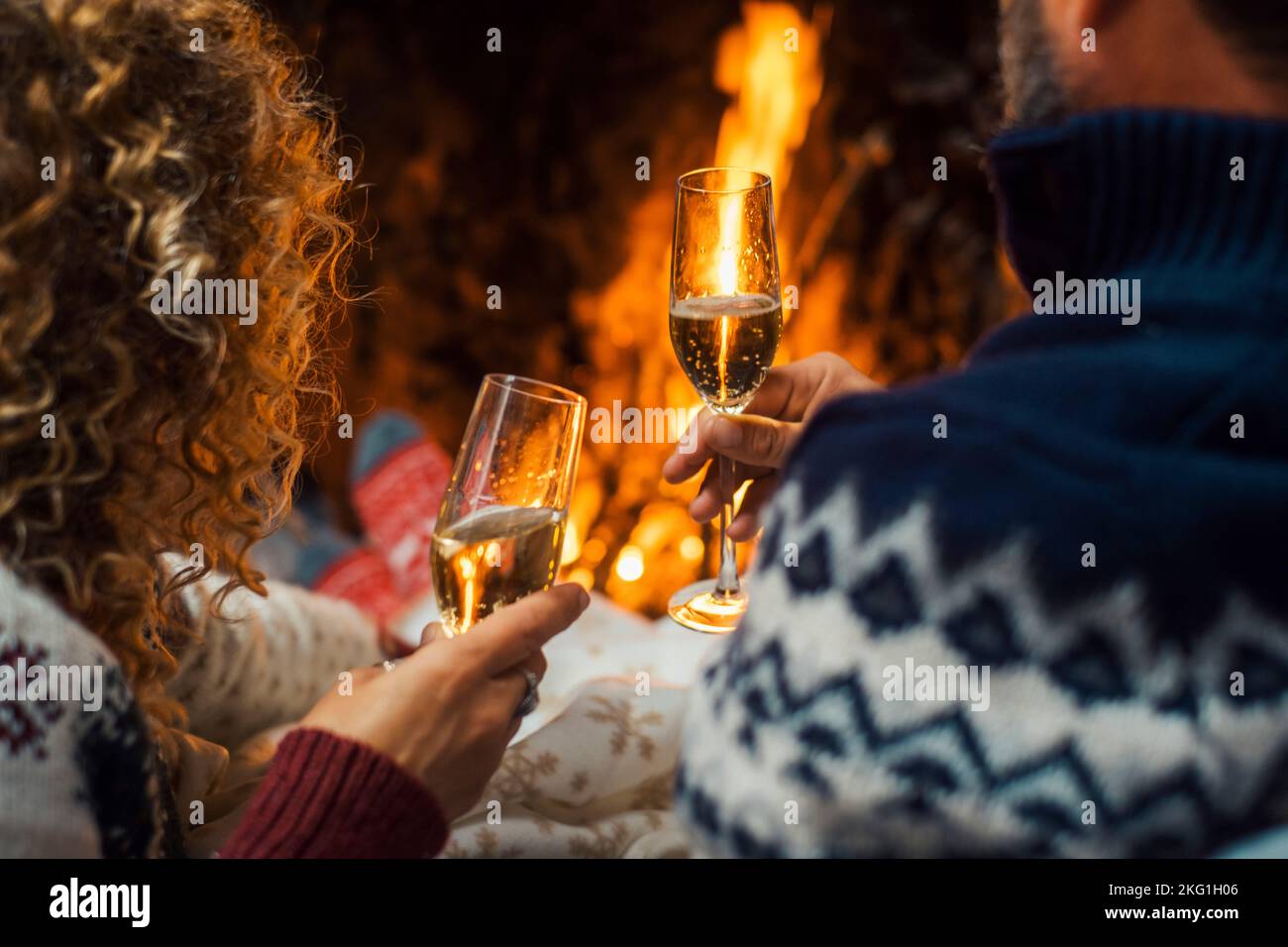 Back view of couple enjoying and celebrating together clinking with champagne flutes inside home with fireplace in background. Winter holiday season a Stock Photo