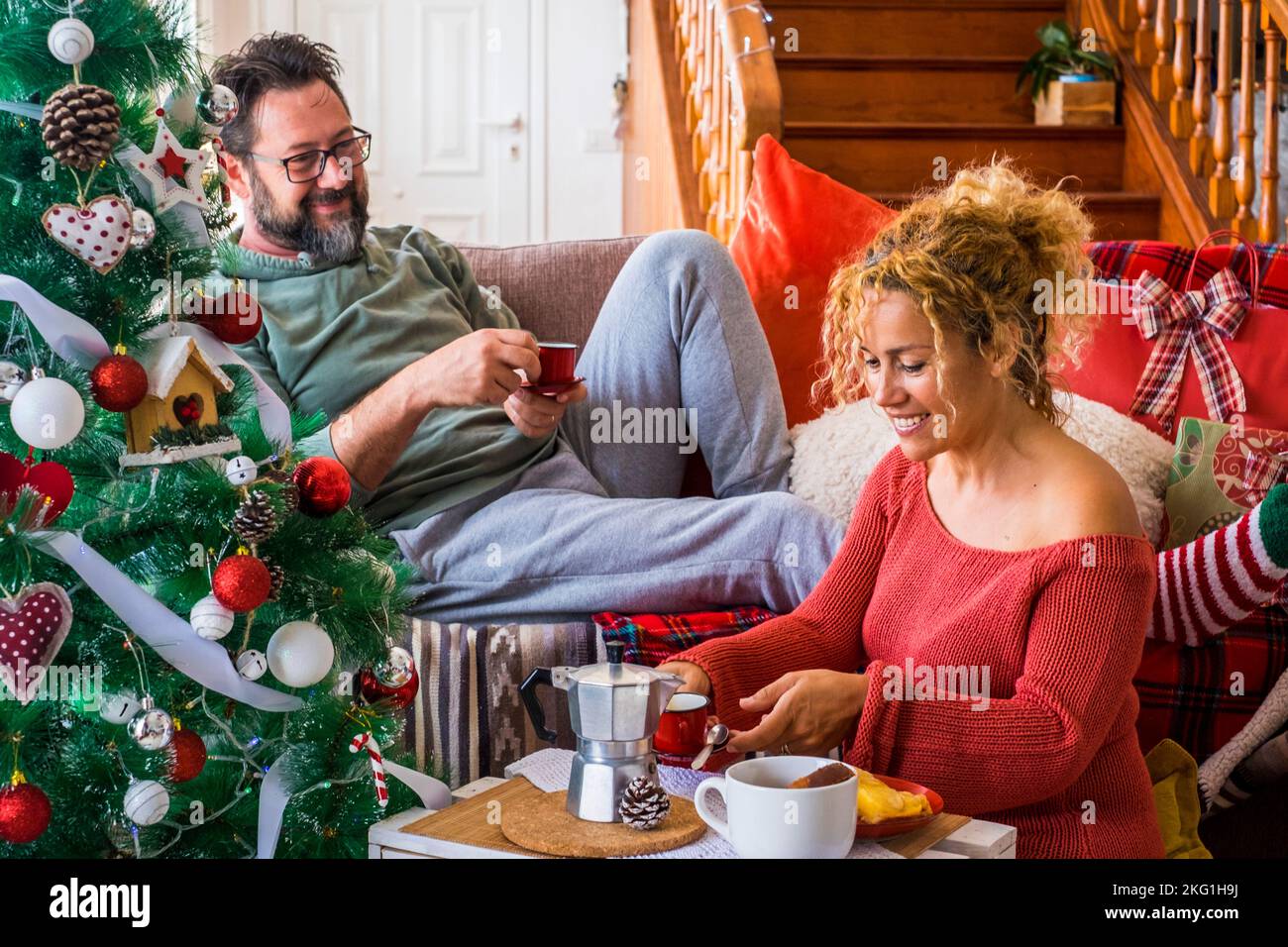Happy couple family man and woman enjoy christmas holiday morning at home having breakfast together. Xmas tree and coffee time. December event season. Stock Photo