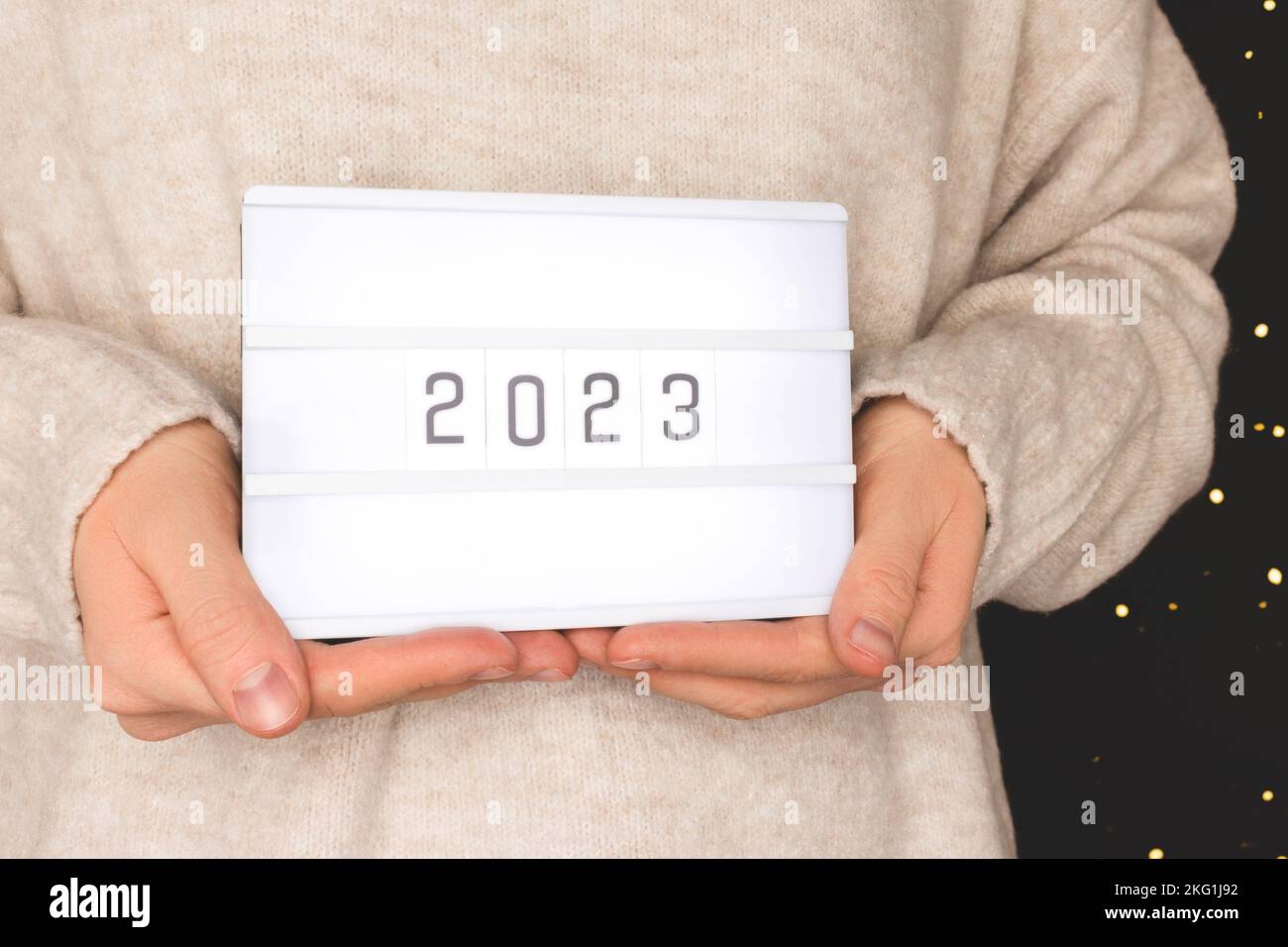Female hands hold lightbox with 2023 numbers in front of black background. New Year concept. Stock Photo