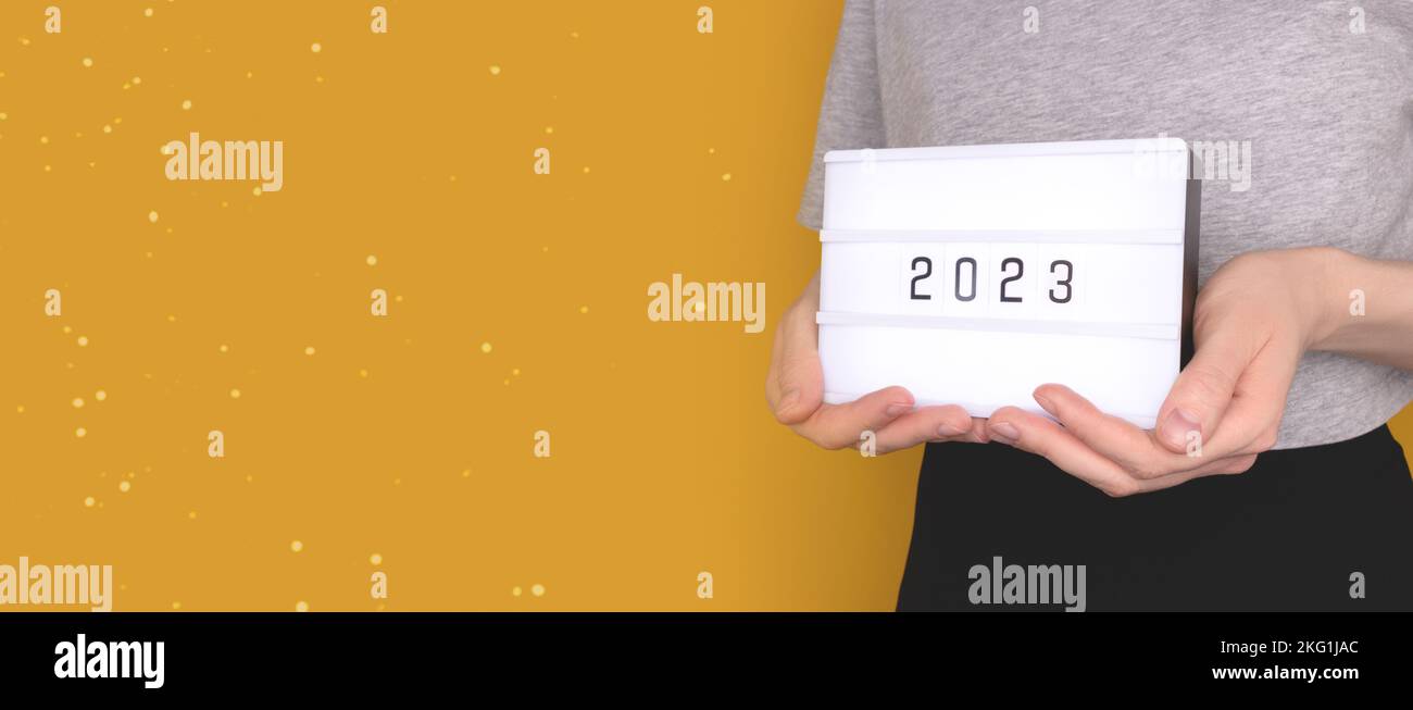 Banner with female hands hold lightbox with 2023 numbers in front of yellow background. New Year concept with place for your design. Stock Photo