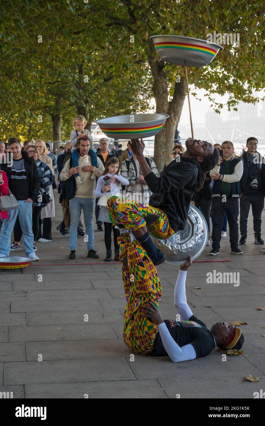 People watch street performers doing balancing and bowl spinning act on South Bank, London, England, UK Stock Photo