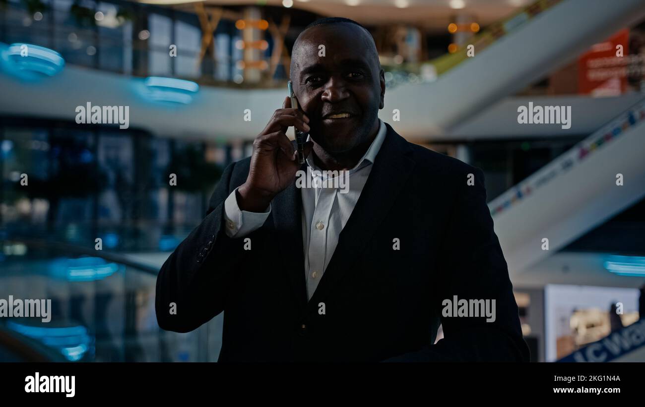 Adult businessman African American middle-aged man employee entrepreneur indoors in office mall company talking phone chatting mobile conversation Stock Photo