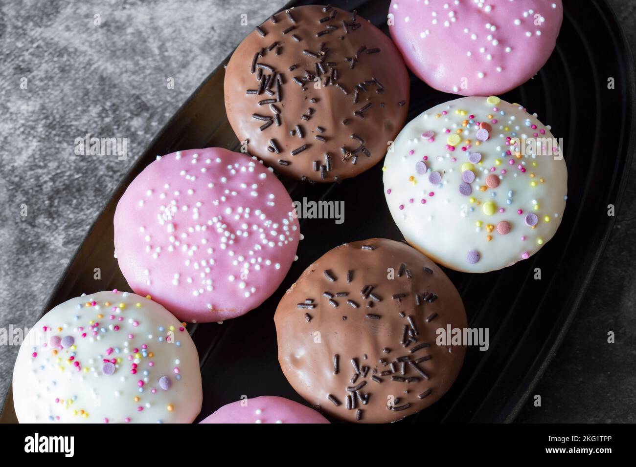 Cupcakes, decorated with icing and sprinkles on a black serving dish. On a dark concrete background Stock Photo