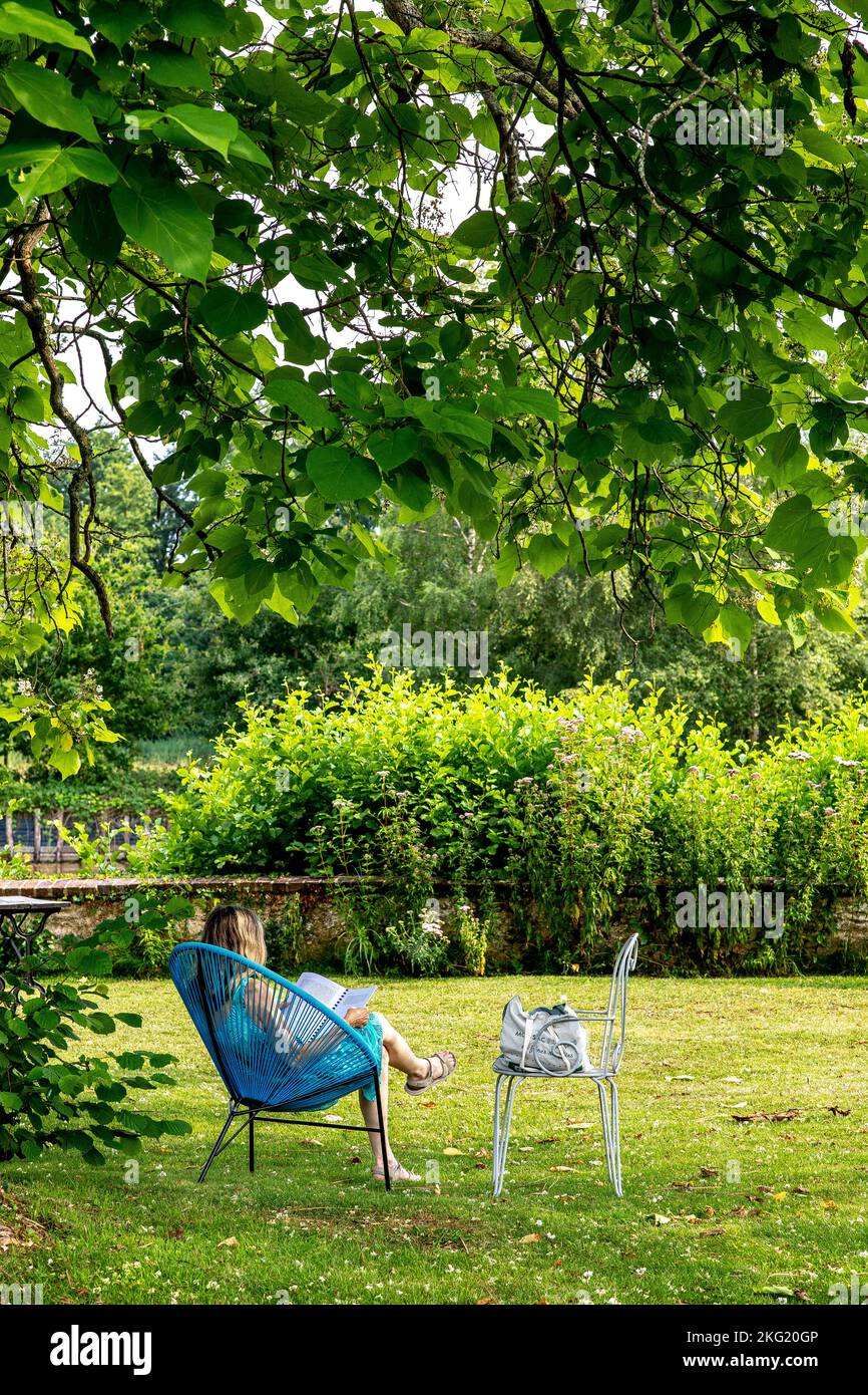 Adults reading in an armchair in a garden in western France Stock Photo