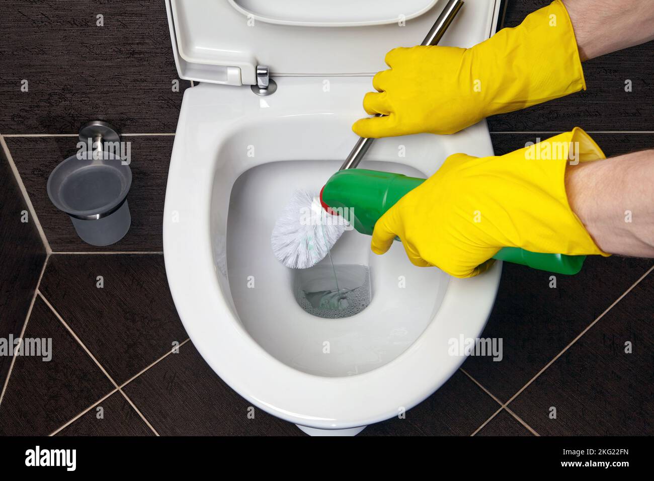 Cleaner in yellow rubber gloves cleans the toilet bowl with a brush and