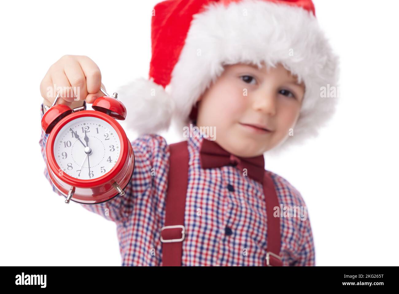 Christmas boy with red alarm clock, smiling little man in red Santa claus hat, tie and suspender posing on white background Stock Photo