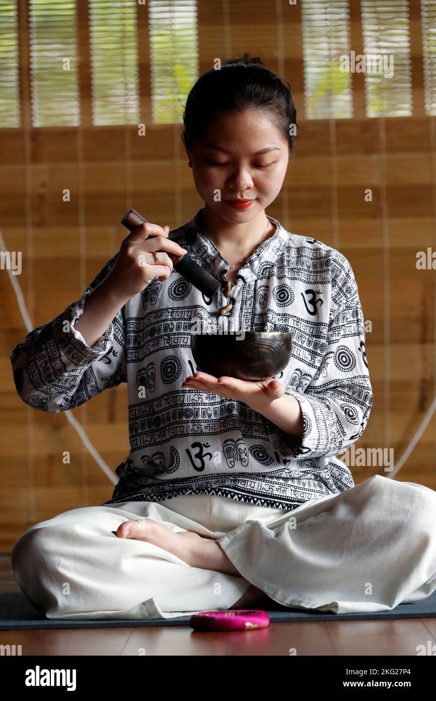 Buddhist woman holding and playing a tibetan singing bowl with a wooden