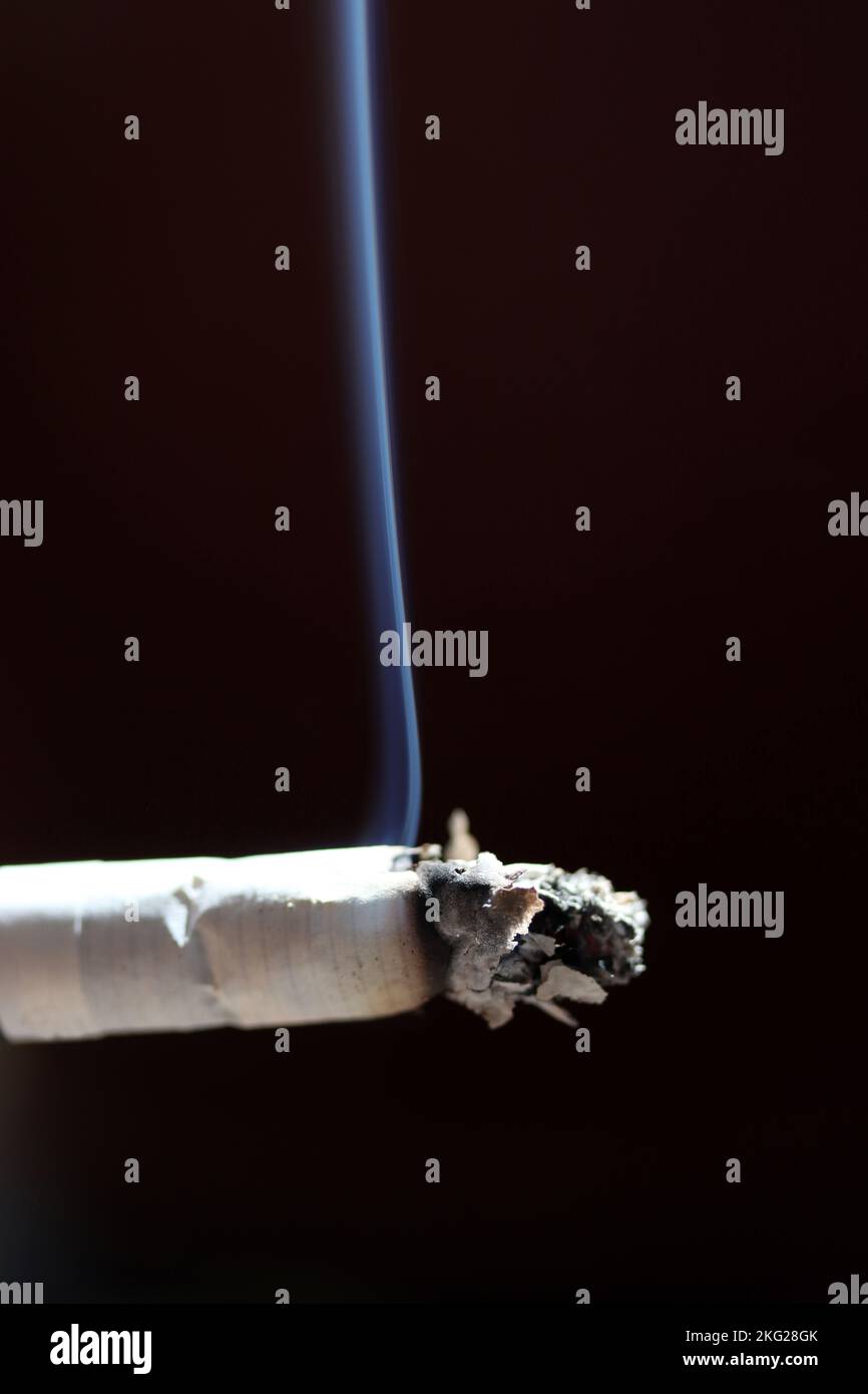 Closeup of burning cigarette with smoke against black background Stock