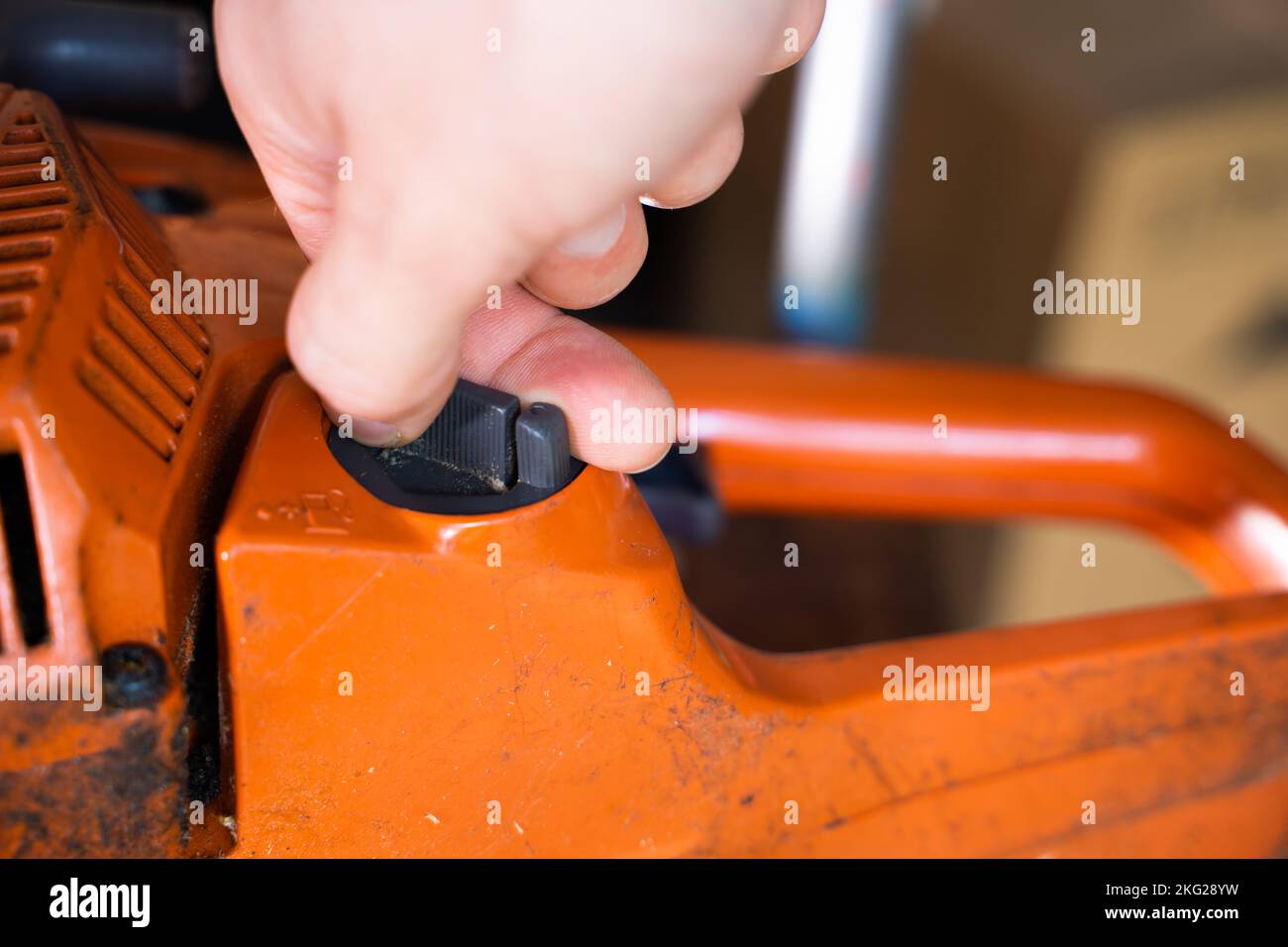 A hand unscrews the cap of the fuel mixture tank in an orange chainsaw