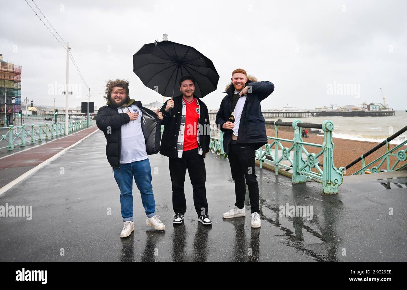 Brighton UK 21st November 2022 - England fans battle the wind and rain on Brighton seafront as they make their way to a bar to watch the Qatar World Cup match between England and Iran today : Credit Simon Dack / Alamy Live News Stock Photo