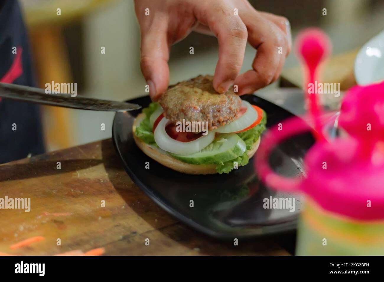 Chef puts beef patty for burger filling, on kitchen utensils background