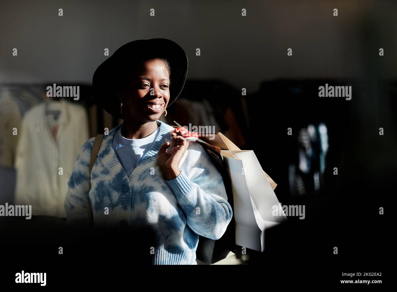 Trendy portrait of smiling black woman holding shopping bags in thrift ...