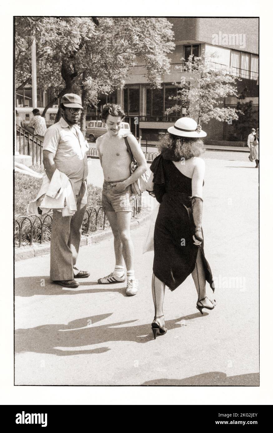 LEERING. 2 young man stare at an unusually dressed woman. In Washington Square Park in Manhattan, New York City, circa 1979. Stock Photo