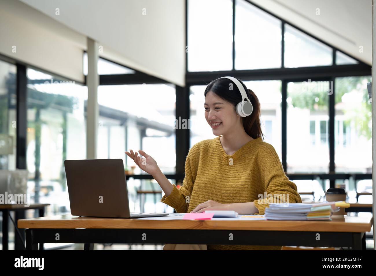 Happy young asian girl with wireless headphones looking at laptop