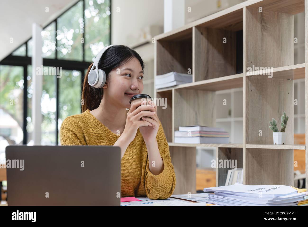 Happy young asian girl with wireless headphones looking at laptop