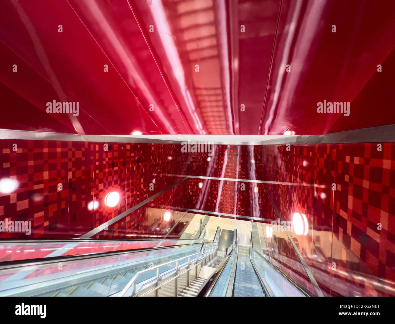 Inside an underground train station. A long escalator travel deep down in red colour wall interior design. Stock Photo