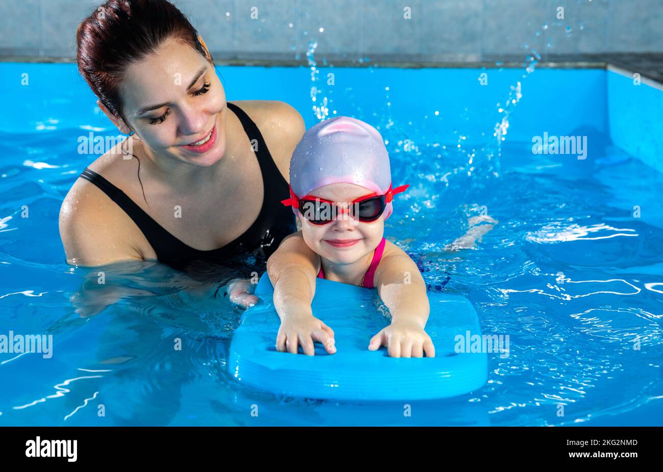 Woman teaching little girl how to swim in indoor pool with pool