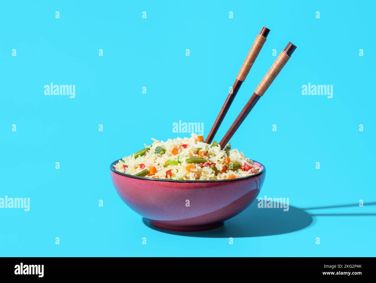 Close-up with a bowl with fried rice dish and chinese chopsticks. Delicious asian dish, fried rice with a mix of chopped vegetables, minimalist on a b Stock Photo
