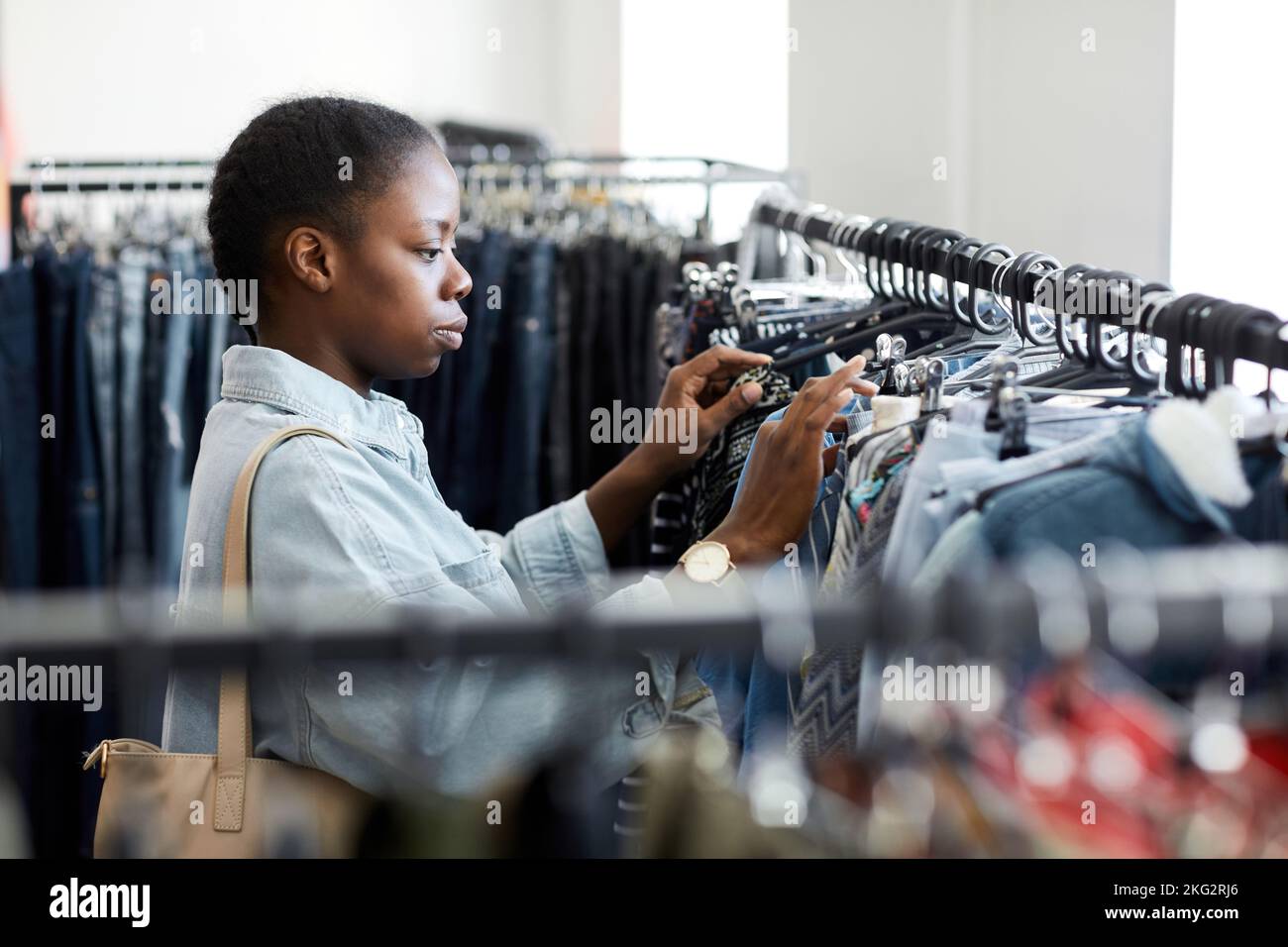 Side view portrait of black young woman looking at clothes on rack in second hand store Stock Photo